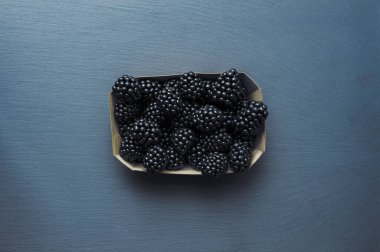 Gri desenli masada duran kağıt kutunun içindeki böğürtlen yığınının üst görüntüsü. Taze meyve konseptinde vitaminler.