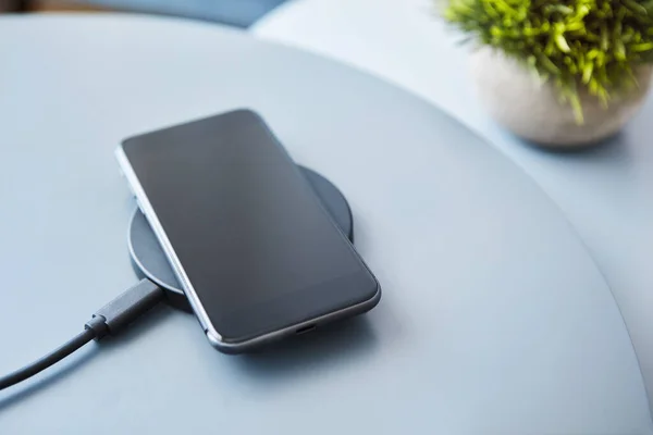 Wireless inductive charging smartphone battery. Electronic communication device against light blue background. Modern technology, wireless device and transfer of energy concept.