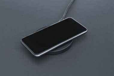 Kablosuz şarj cihazıyla şarj olurken lüks akıllı telefonun yakın plan görüntüsü. Arka planda Matt Grey masa yüzeyi var. Modern teknoloji, kablosuz aygıt ve enerji aktarımı.