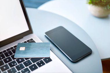 Laptop, elektronik çip kartı ve mavi yuvarlak masada akıllı telefon. İnternetten ödeme ya da müşteri kimliği. Modern teknoloji, kablosuz aygıt ve enerji aktarımı.