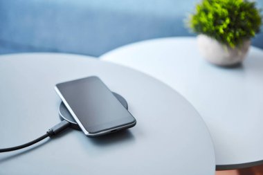 Kablosuz indüktif akıllı telefon pili. Açık mavi arka plana karşı elektronik iletişim cihazı. Modern teknoloji, kablosuz aygıt ve enerji aktarımı.