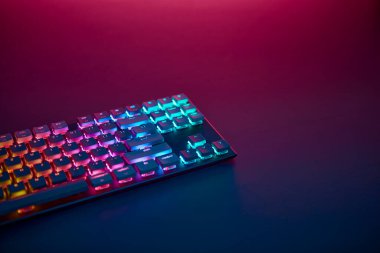 Masada gökkuşağı rengi arka planda oyun klavyesi var. Yukarıdan gelen mor ışık. Profesyonel bilgisayar oyunu, esport işi ve online dünya konsepti.
