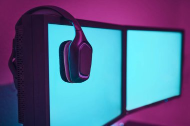 Kablosuz kulaklıklar bilgisayar ekranında asılı. İçeriğinizi eklemek için boş monitör. Profesyonel bilgisayar oyunu, esport işi ve online dünya konsepti.
