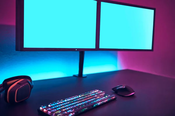 Two high resolution displays, keyboard with colorful illumination and gaming mouse. Blank monitor to insert your content. Professional computer game playing, esport business and online world concept.