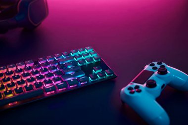 Gökkuşağı rengi arka planda oyun klavyesi, oyun sahası ve müzik kulaklığı. Yukarıdan gelen mor ışık. Profesyonel bilgisayar oyunu, esport işi ve online dünya konsepti.