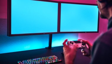 Omzunun üstünden oyun kumandasını tutan ve ikili ekranda oynayan adamın görüntüsü. İçeriğinizi eklemek için boş monitör. Profesyonel bilgisayar oyunu, esport işi ve online dünya konsepti.