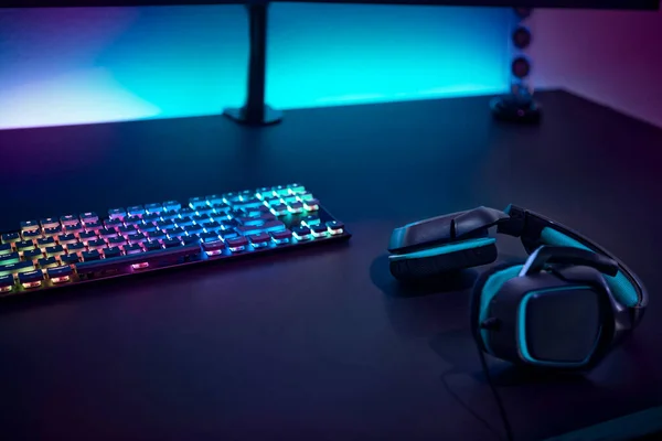Gaming accessories on dark table. Keyboard with color backlit and stereo headphones. Professional computer game playing, esport business and online world concept.