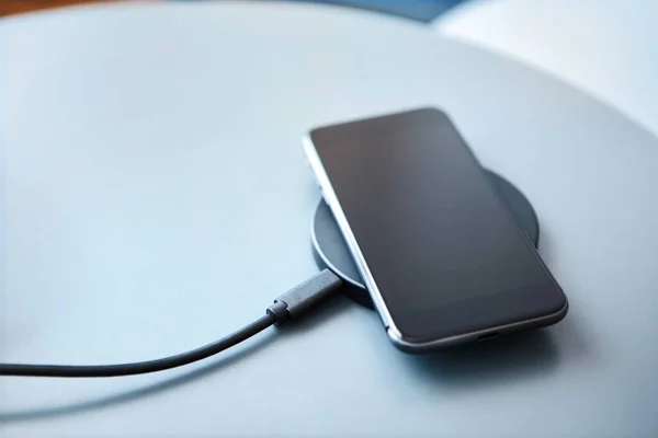 Charging smartphone on round wireless charging pad. Modern technology, wireless device and transfer of energy concept.