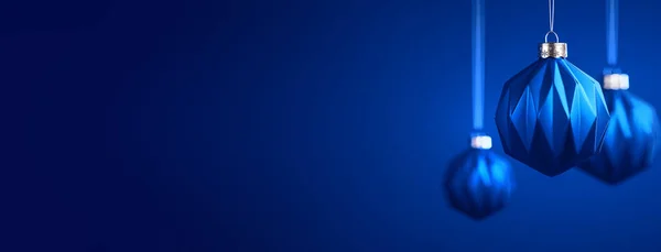 Kraliyet mavi arka planına karşı üç Noel balosu. Modern geometrik desenli Matt Blue mücevherleri. Noel dekorasyonu, şenlikli atmosfer konsepti. Boşluğu kopyala.