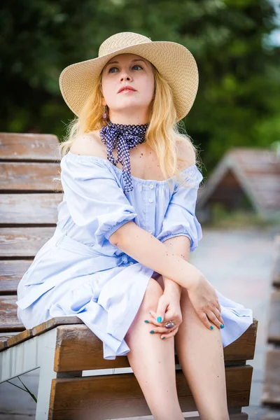 穿着蓝色衣服的金发姑娘 戴着漂亮的帽子 躺在城市公园的长椅上 — 图库照片