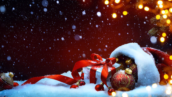 Santa Claus red bag with Christmas balls and gift box on snow