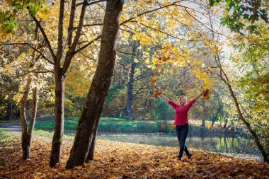 Mutlu kadın parka sonbahar yaprakları kusar. Çekici sarışın beyaz bir kadının portresi altın sonbahar mevsiminin tadını çıkarıyor.