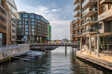 Oslo, Norveç - 16 Temmuz 2025: Günümüz konut ve ofis binaları güneşli bir yaz öğleden sonrasında rıhtımda demirlemiş teknelerle Aker Brygge rıhtımında hizmete girerler..