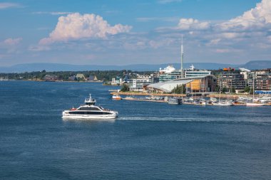 Oslo, Norveç - 16 Temmuz 2025: Modern bir toplu taşıma feribotu Oslofjord 'dan geçiyor, şehrin manzaralı limanı ve güneşli bir günde arka planda bir marina var..