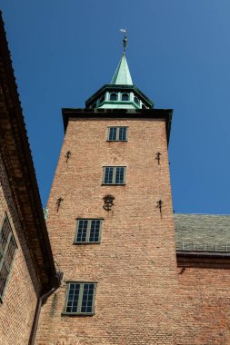 Oslo, Norveç - 16 Temmuz 2025: Yeşil bakır kulesi olan tarihi kırmızı tuğla kule, Ortaçağ kent simgesi Akershus Kalesi 'nde açık mavi gökyüzüne karşı duruyor.