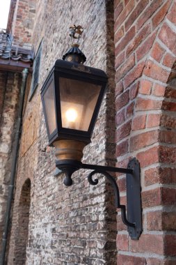 Oslo, Norveç - 16 Temmuz 2025: Oslo 'daki tarihi Akershus Kalesi' nin yıpranmış tuğla duvarını süsleyen, eski tarz bir sokak lambası aydınlatıyor.