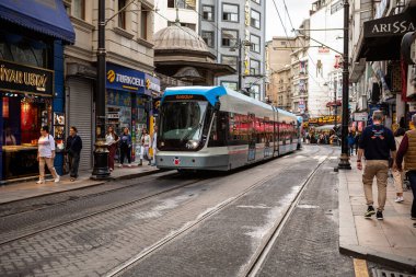 İstanbul, Türkiye - 5 Ekim 2025: Günümüz tramvayı, kentin tarihi ticaret merkezinde bir sonbahar günü mağazalar ve yayalarla dolu işlek bir cadde boyunca seyahat ediyor.
