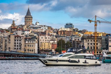 İstanbul, Türkiye - 5 Ekim 2025: Altın Boynuz su yolu üzerinde tarihi Galata Kulesi ve Beyoğlu ilçesinin manzarasıyla lüks bir yat seyahat ediyor.