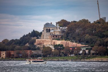 İstanbul, Türkiye - 5 Ekim 2025: Seraglio Noktası 'ndaki tarihi Topkapı Sarayı manzaralı bir tur teknesi, bulutlu bir sonbahar gökyüzü altında İstanbul Boğazı üzerinde seyahat ediyor.
