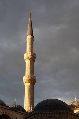Tarihi Mavi Cami 'nin (Sultan Ahmed Camii) süslü taş minaresi, İstanbul, Türkiye' de dramatik bir gökyüzüne karşı altın saat ışığıyla aydınlanıyor