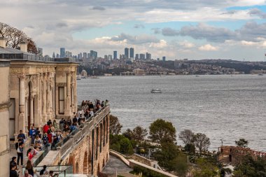 İstanbul, Türkiye - 4 Ekim 2025: Turistler, bulutlu bir sonbahar gününde İstanbul Boğazı ve uzak modern ufuk çizgisini görmek için Topkapı Sarayı 'nda bir terasta toplandılar.
