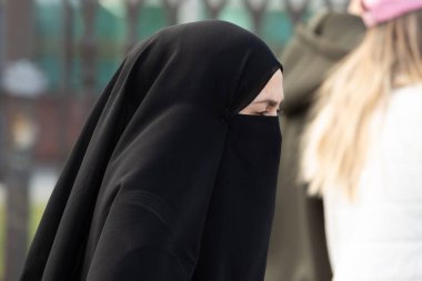 İstanbul, Türkiye - 5 Ekim 2025: Bir kadın, bir sonbahar günü İstanbul 'da halka açık bir alanda yürürken, sadece gözleri görünen siyah bir takı takıyor.