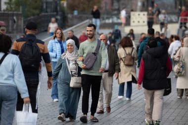 İstanbul, Türkiye - 5 Ekim 2025: Başörtülü genç bir çift, kalabalık bir meydanda yürüyor ve gülümsüyor, kentin çeşitli ve hareketli toplumunu temsil ediyor.