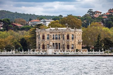 İstanbul, Türkiye - 5 Ekim 2025: Osmanlı İmparatorluk av kulübesi süslü Kucuksu Sarayı (Kucuksu Kasri), bulutlu bir sonbahar gününde, tepenin yamaçlarındaki yeşilliklerle çevrili, Boğaz 'ın Asya kıyısında yer alır..
