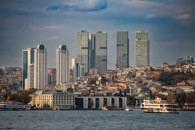 İstanbul, Türkiye - 5 Ekim 2025: Günümüz Levent ve Sisli gökdelen silueti, Boğaz önplanında tarihi bir yapı ve feribot ile arka plana hakim.