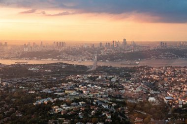 Gün batımında İstanbul 'un tamamının engin, puslu panoramik manzarası ön plandaki kalabalık Asya yakasını, Boğaz' ı ve uzak mesafedeki kümelenmiş Avrupa gökdelenlerini gösteriyor..