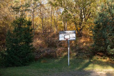 Litvanya 'nın Vilnius kentindeki Paneriai semtinde, sararmış yapraklı ağaçlar ve yemyeşil ağaçlarla çevrili, yıpranmış bir basketbol sehpası ve çember sakin bir düzlükte oturmaktadır.