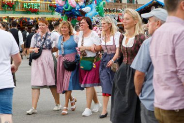 Münih, Almanya - 21 Eylül 2023: Çeşitli geleneksel Bavyera Dirndl giysileri giyen bir grup kadın, Ekim Festivali sırasında kalabalık Theresienwiese 'de kollarını kavuşturarak yürüyorlar..