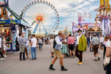 Münih, Almanya - 21 Eylül 2023: Bulutlu bir gökyüzü altında kalabalık Theresienwiese panayırı üzerinde yükselen ikonik dev dönme dolap manzarası.