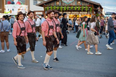 Münih, Almanya - 21 Eylül 2023: Geleneksel Bavyera deri pantolon ve kareli gömlekli bir grup adam, geleneksel Oktoberfest kutlamaları sırasında festival sahasında yürüyor.
