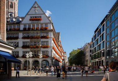 Münih, Almanya - 21 Eylül 2023: Kaufinger Caddesi boyunca yürüyen yayalar, şehir merkezindeki Frauenkirche katedrali yakınlarında kırmızı çiçeklerle süslenmiş ikonik Hirmer binasının önünden geçtiler.