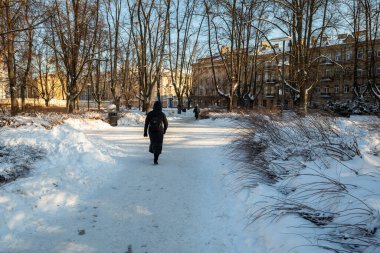 Vilnius, Litvanya - 01 Şubat 2026: Bir kişi Lukiskes Meydanı 'nda karla kaplı bir patika boyunca yürür parlak bir kış öğleden sonra çıplak ağaçlarla çevrili.