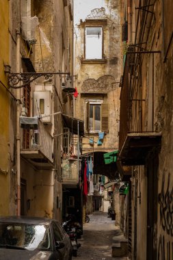 Napoli, İtalya - 4 Kasım 2022: Bir kişi dar bir sokak aralığında balkondan dışarı bakıyor ve çamaşırhanelerde asılı ve yıpranmış tarihi binalar var.