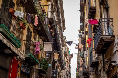 Napoli, İtalya - 4 Kasım 2022: Renkli çamaşırlar, tarihi şehir merkezinde yıpranmış bina cepheleri ile dar ve uzun bir yerleşim yeri caddesi boyunca uzanan çamaşır iplerine asılı duruyor.