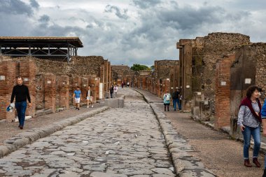 Pompei, İtalya - 5 Kasım 2022: Ziyaretçiler Pompei Arkeoloji Parkı 'nda tuğla kalıntıları ve sayılı kazılarla kaplı antik Roma caddesini keşfediyorlar..