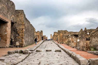 Pompei, İtalya - 5 Kasım 2022: Pompei Arkeoloji Parkı 'ndaki yayalar için antik yükseltilmiş basamakların yer aldığı asfalt bir Roma caddesi boyunca yürüyen ziyaretçiler.
