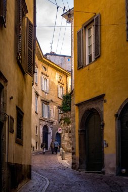 Bergamo, İtalya - 7 Kasım 2022: Yayalar Citta Alta ilçesinde renkli tarihi binalar ve taş kemerlerle çevrili dar, dolambaçlı bir kaldırım boyunca yürürler.