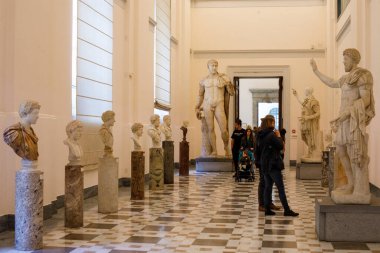Napoli, İtalya - Kasım 06, 2022: Ziyaretçiler, Ulusal Arkeoloji Müzesi 'ndeki antik Roma mermer portre büstleri ve anıtsal heykellerle dolu uzun bir galeride yürüyorlar.