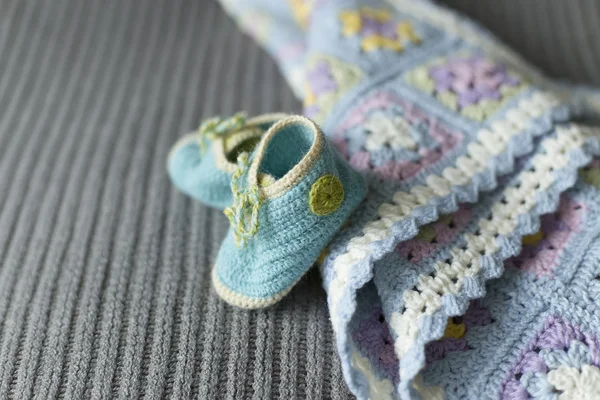 Hand knitted baby booties and blanket on the soft grey surface — Stock Photo, Image