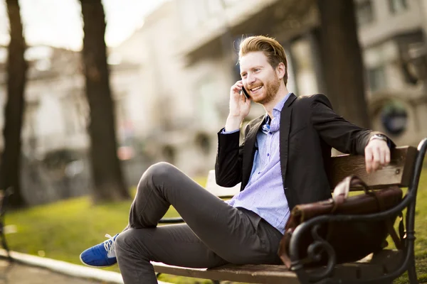 Junger Mann mit Telefon auf Bank — Stockfoto