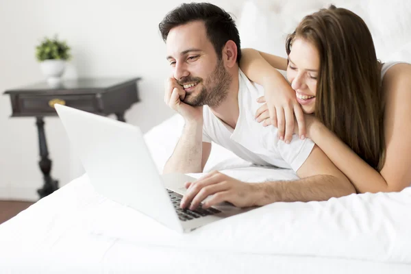 A fiatal pár az ágyban laptop — Stock Fotó