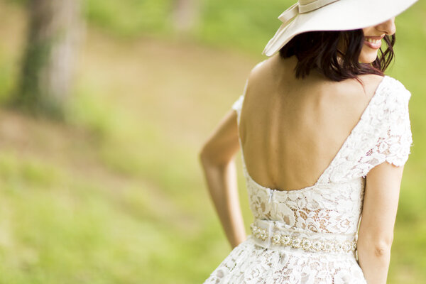 Young woman posing in a white dress with a hat in summer park