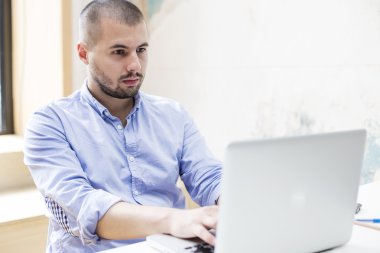 Dizüstü bilgisayarda çalışan genç adam.