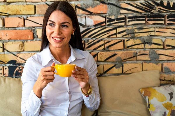 Pretty young woman with mug in hands drinking coffee in the morning at restaurant