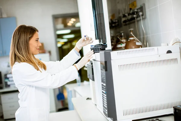 身穿白色实验室外套的年轻女科学家把小瓶和样本放在生物医学实验室的气相色谱法中进行分析 — 图库照片