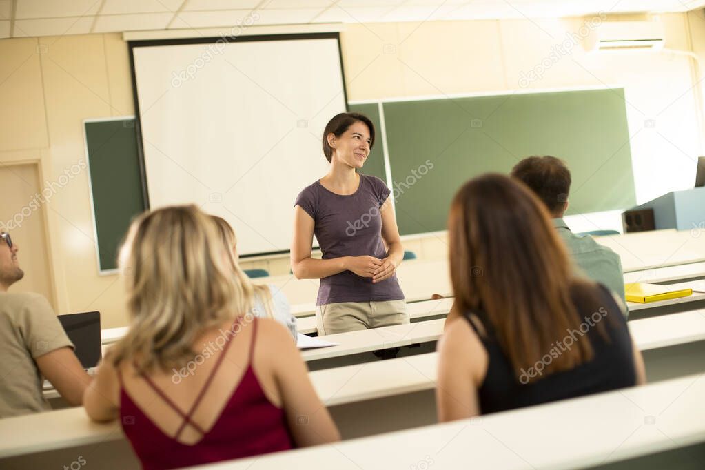 Group of university students in the classroom with young female assistant lecturer